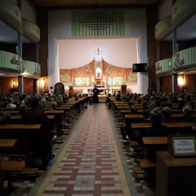 Uczniowie klas wczesnoszkolnych siedzący w ławkach i słuchający Księdza Jacaka Banasiuka. 