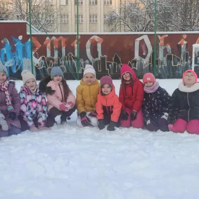 Uczennice klasy 1a siedzące w śniegu podczas porannej gimnastyki na boisku szkolnym 