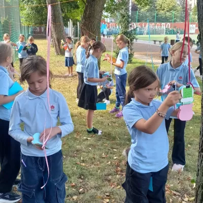 Uczennice klasy 3c czytają swoje wakacyjniki rozwieszone na szkolnym boisku
