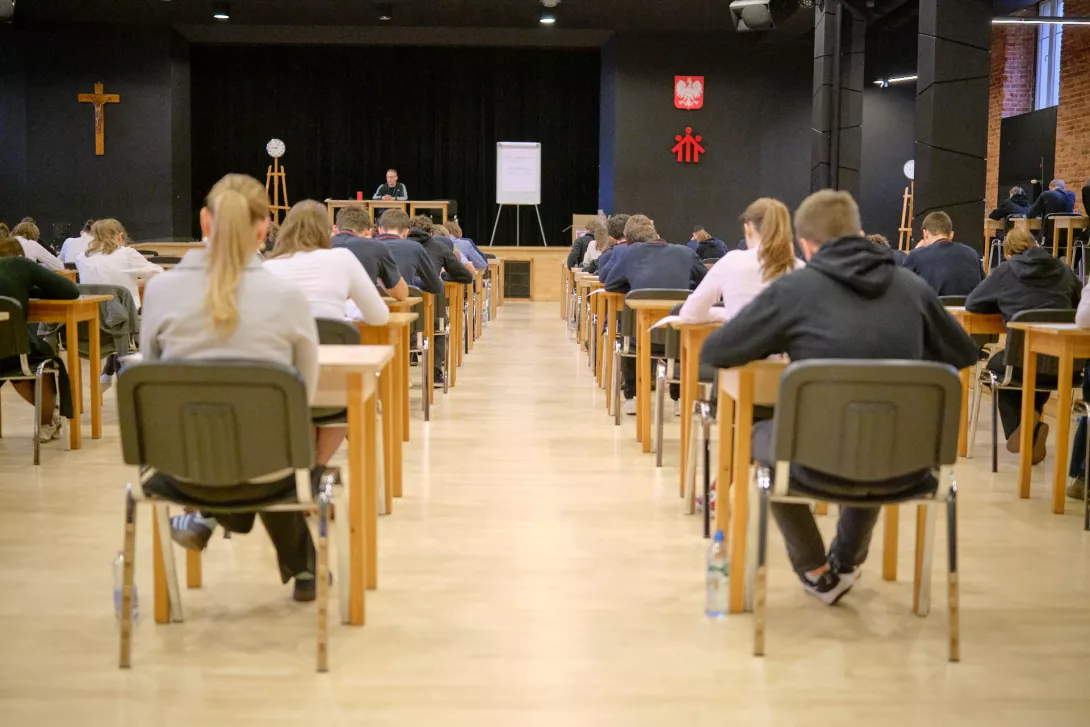 Maturzyści piszą w Auli szkolnej próbny egzamin maturalny.