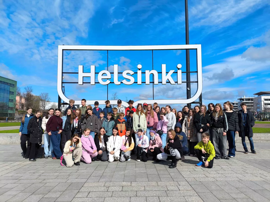 Zdjęcie grupowe uczestników wycieczki przed napisem Helsinki obok biblioteki Oodi w Finlandii.