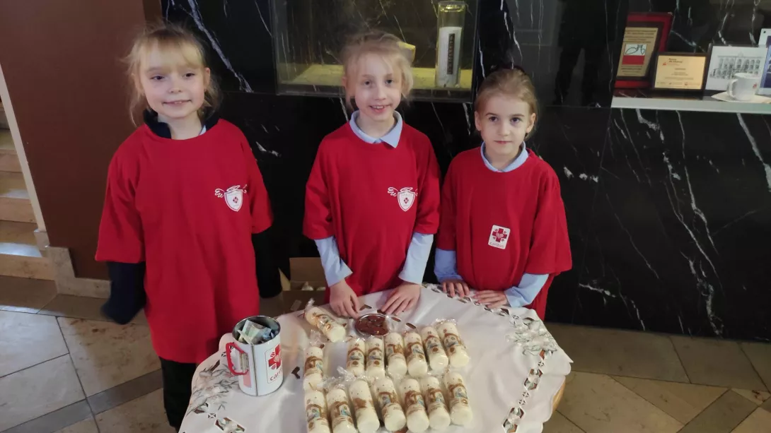 Wolontariuszki SKC sprzedające świece w szkolnym holu w ramach akcji Wigilijne Dzieło Pomocy Dzieciom Caritas Polska w dniach 14-16 grudnia 2025