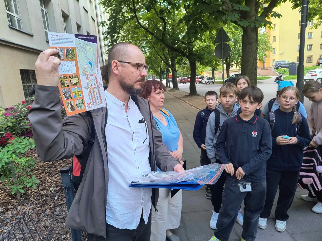 Uczniowie klas piątych w czasie gry terenowej słuchający przewodnika przed naszą szkołą