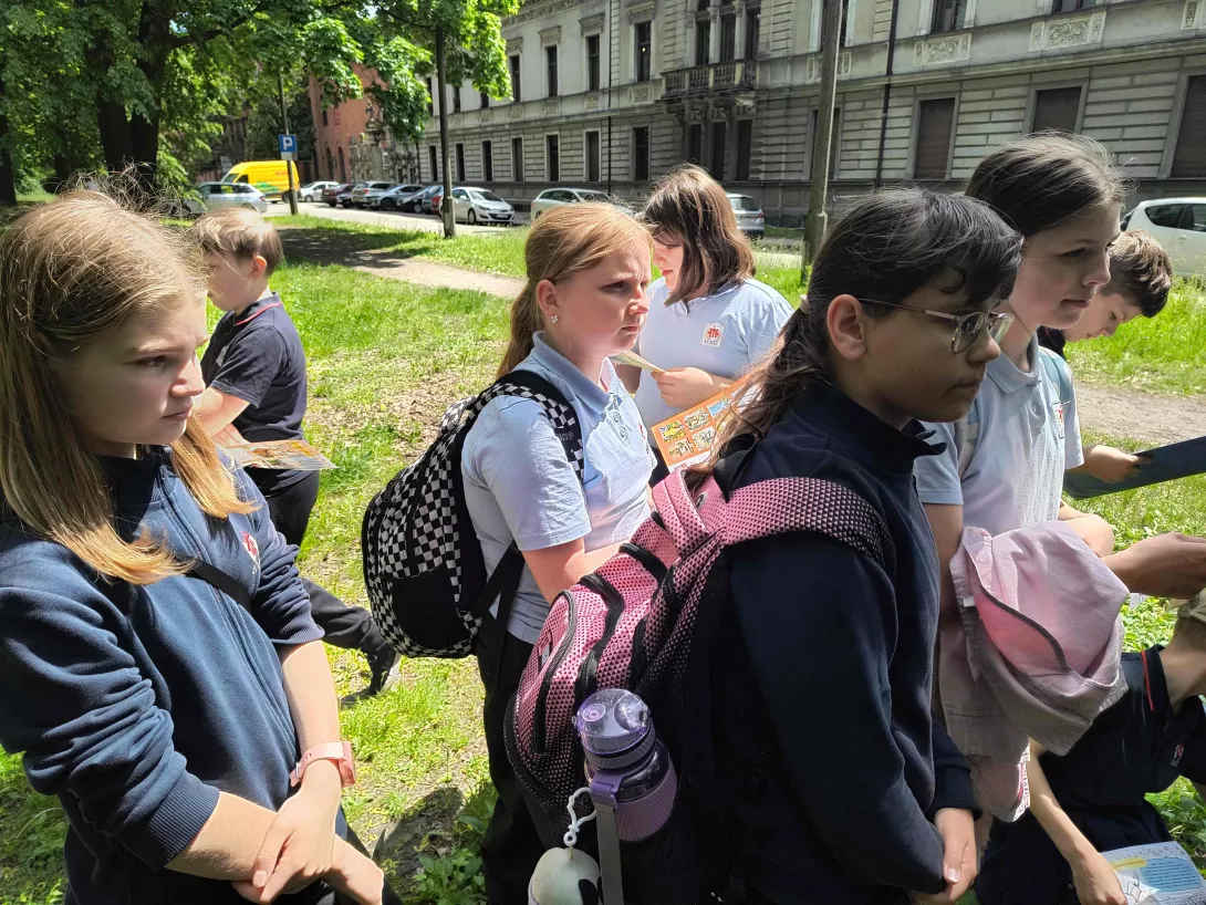 Uczniowie klas piątych w czasie gry terenowej słuchający przewodnika przed pałacem  Karola Scheiblera