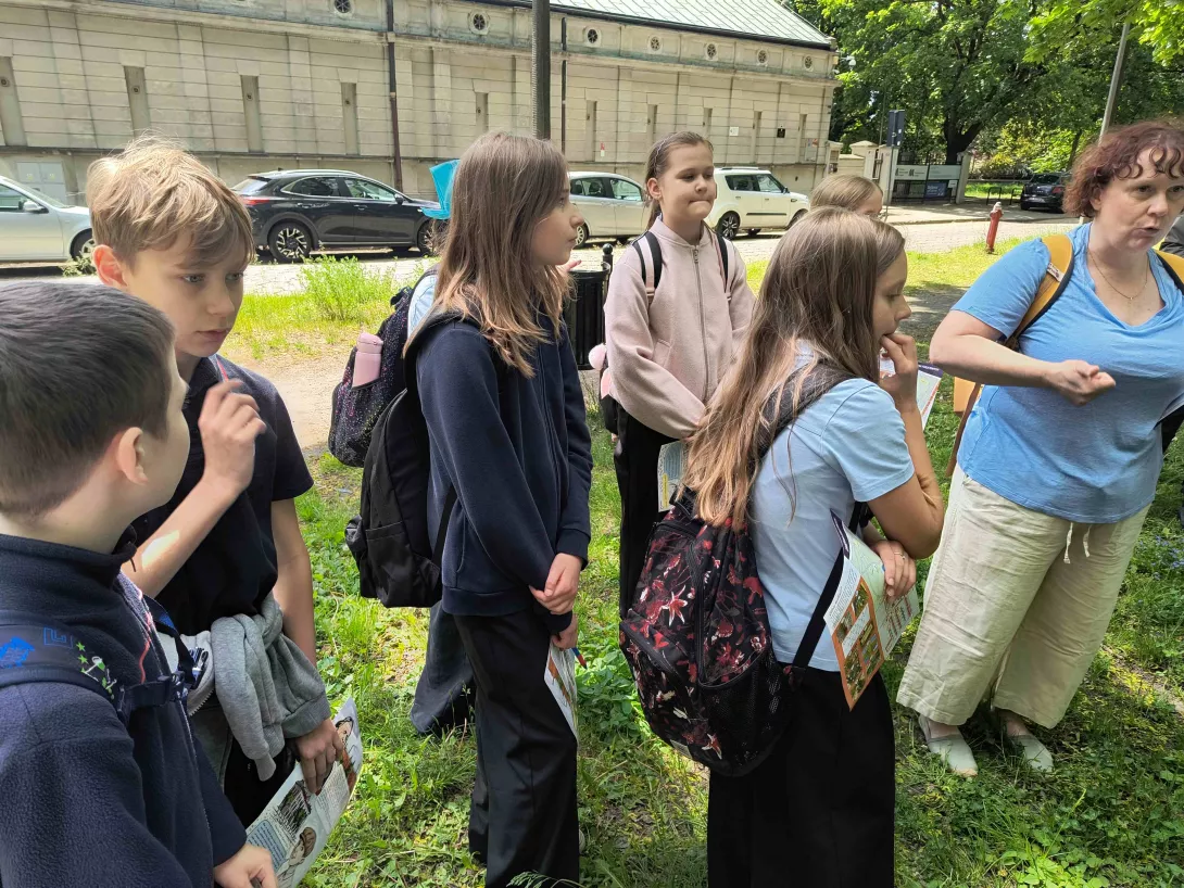 Uczniowie klas piątych w czasie gry terenowej słuchający przewodnika przed pałacem Scheiblera