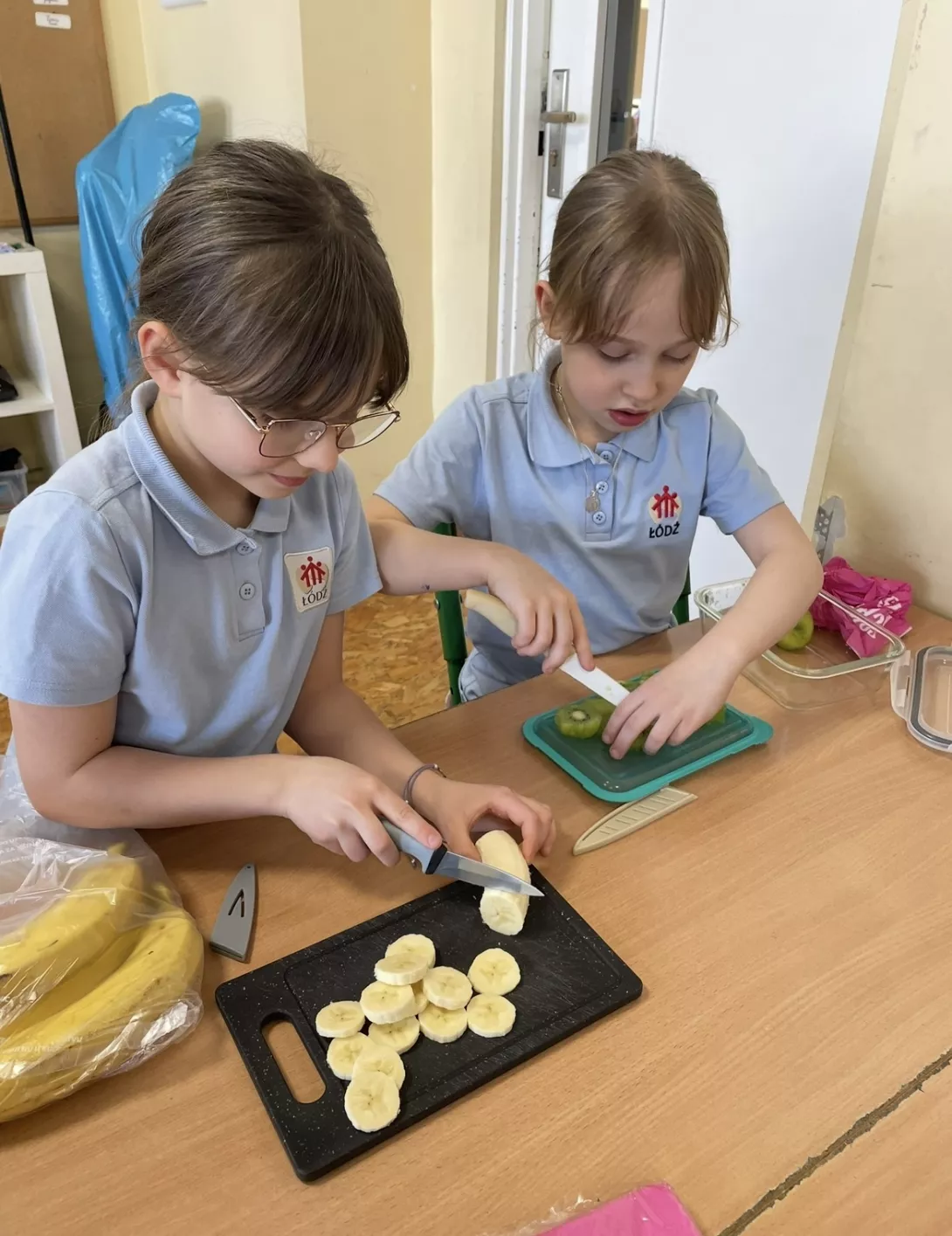 Uczennice przygotowują sałatkę owocową.